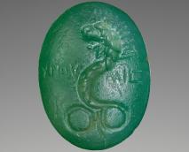 Oval stone engraved on each of its sides. On the obverse is the image of a lion-headed Chnoubis serpent, crowned by twelve rays. Horizontal inscriptions flank each side of the figure: XNOY __ MIS (Chnoumis, a variant for Chnoubis). On the reverse is a Chnoubis-sign (three parallel crooked lines with a crossbar running through them).