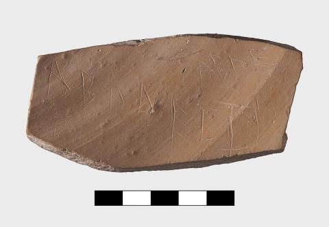 An oblong fragment of a red clay vessel with two lines of Greek lettering.