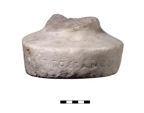 A round marble base, with stumps broken off on the top and a single line of Greek lettering across the front face