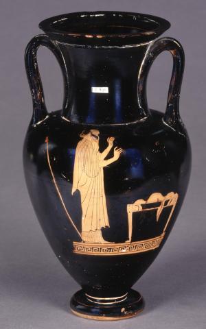 Phineus stands to the left of an offering table. His hands are raised in supplication. He is bearded and bald on top, with curls hanging down the back of his head. He wears a headband, long-sleeve chiton and mantle. Behind him his scepter stands upright and leaning slightly, as if against a wall. The tabletop is covered with offerings, part of which hangs over the side.