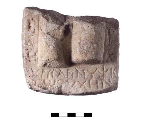 A marble fragment with two vertical cylinders and two lines of Greek lettering beneath them.