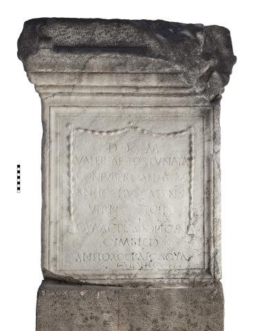 A marble monument base with lines of Latin lettering on the top half and lines of Greek lettering on the bottom half.