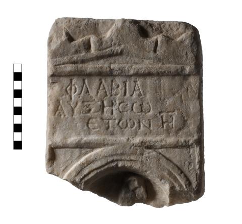 A marble fragment with lines of Greek lettering in the middle and a fragment of a niche at the bottom.