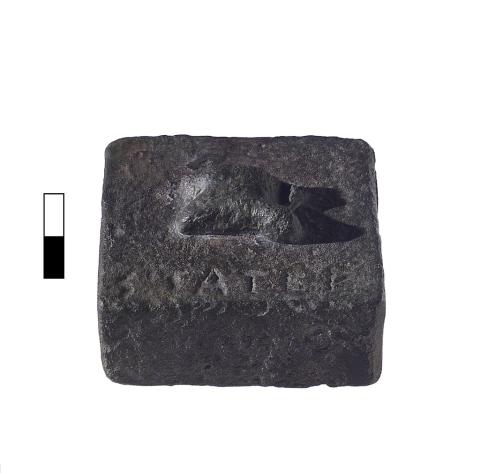 A rectangular bronze block with a relief in the center and a single line of Greek lettering.