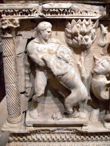 Hercules (center) grapples with the Nemean Lion. The lion stands on his hind legs head turned into Hercules' left shoulder with its left front paw clawing Heracles' right arm. The pair are flanked by a spiral carved column (left) and a tree (right).