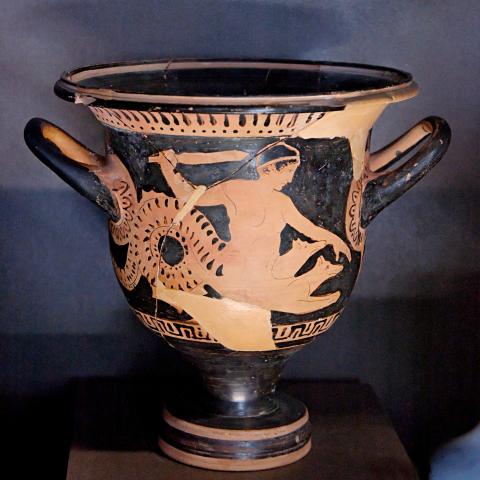 Scylla, in profile facing right, raises a sword in her right hand. She is shown with the nude torso of a human woman merged with a sea serpent tail. She also has the front half of two dogs emerging from her abdomen.