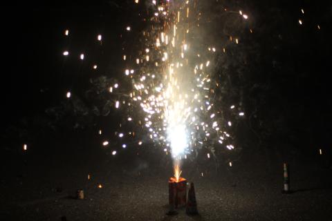 A rectangular canister sits on concrete and shoots sparks into the air.