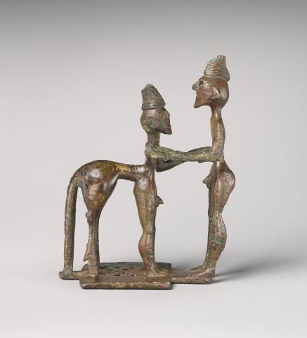 Picture of a bronze figurine of a centaur and man in profile. The man stands on the right; the centaur on the left. They grasp each other by the arms. The centaur has human front legs and a horse's rear legs and tail. They are both nude and wear some sort of coiled conical hat or hairstyle on the top of their heads.