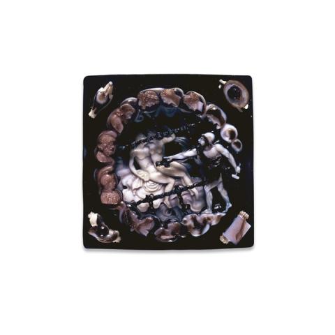 Square onyx and sardonyx cameo. In the center, Vulcan stands on the right wearing a dark tunic and white cap. He holds a hammer in his left hand and gestures with his right hand toward Venus and Mars shown nude, lying on a bed. Overlaying the image are the dark ropes of a net in which Vulcan has captured the lovers. Encircling the scene are several busts representing the other Olympian gods. The artist has engraved his name, D. Calabresi, across one of the ropes forming the net. 