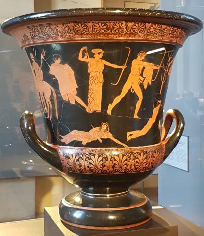 Artemis (center), dressed in a peploswwith hair drawn into a a bun and covered, draws an arrow from a quiver on her back with her right hand, holding her bow outstretched in her left. Apollo (right) knocks an arrow to his bow in his left hand, arrow in his right. He is nude and his quiver is slung across his body on his left hip. A cloak is wrapped around his left arm. At their feet a woman and man lay peirced by arrows. To the left of Artemis another young kneels, pierced by an arrow.