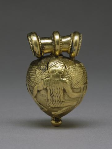 Rounded amulet with slightly pointed bottom, showing a winged man. He wears a vertical folded or striped tunic. His knees are bent as if squatting.