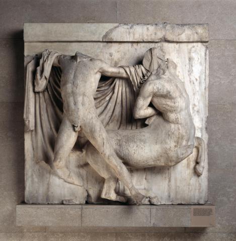 A centaur appears to be fleeing right, but is held back by a man facing full front. The centaur's right arm is twisted behind his back, as if reaching for something. His left arm is raised, but is missing from the bicep, as is the centaur's head. The man appears to be grasping the centaur by the back of the head with his left hand. The man's right arm is missing from the bicep, but is raised as if about to strike. His head is also missing, and he is nude except for a cloak draped behind him.