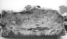 External stone platform, badly corroded and chipped, with a line of four Greek letters