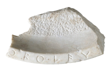 An irregularly shaped white marble fragment with a line of Greek lettering along the rim