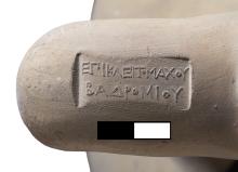 A section of a clay vessel with a stamp in the middle, containing two lines of Greek lettering.