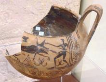 A broken pottery vessel, most of the left side is missing. The interior has been glazed with a dark pigment. The handle on the right side is preserved. Two bands of decoration are visible on the body. The bottom a series of nested circles, each comprising 7 rings and adot in the center. The upper band shows a man and four-legged animal, in silhouette, fighting. The animal faces right, teeth bared and tongue showing. The man's sword is in his left hand jabbing toward the animal, scabbard at the waist. 