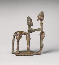 Picture of a bronze figurine of a centaur and man in profile. The man stands on the right; the centaur on the left. They grasp each other by the arms. The centaur has human front legs and a horse's rear legs and tail. They are both nude and wear some sort of coiled conical hat or hairstyle on the top of their heads.