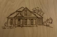 Line drawn woodcut of a house surrounded by bushes and trees. A porch extends across the front of the house supported by wooden beams. A mat sits on the porch in front of the door. 