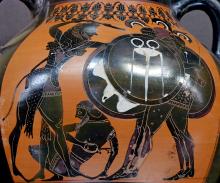 Herakles (left), wearing his lion skin and raising his club with his right hand, fights Geryon (right) depicted with three bodies each in full armor and bearing shields and spears. Eurytion sits on the ground (center) holding his right side with his left hand as if wounded. 