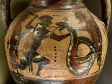 A bearded, armored Cadmus(?) wearing a crested helmet holds a snake or dragon by the neck with his left hand and raises his sword with his right. The snake's mouth is open and its forked tongue is sticking out. On the far right, another bearded and helmeted soldier assists be grabbing the snake from behind. On the far left, behind Cadmus, stands a beared man holding a staff or crook and wearing a cloak.