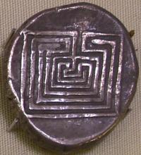 Tarnished round silver coin stamped with the image of a square labyrinth
