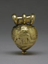 Rounded amulet with slightly pointed bottom, showing a winged man. He wears a vertical folded or striped tunic. His knees are bent as if squatting.