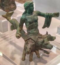 Scylla is shown nude from the waist up with a sea serpent tail and 3 dogs' heads growing from her abdomen. She has a cloak draped over her outstretched left arm. Her fist is closed, probably because she once held an oar, now missing. In her right arm is lowered held slightly out from her side. In her right hand she holds a rock.