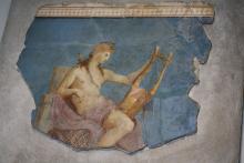 young man seated with chest exposed holding a mid-sized harp