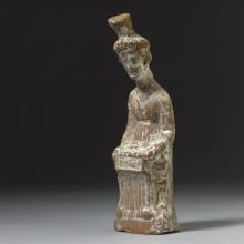 Seated woman dressed in a chiton wearing a cylindrical headpiece known as a polos. In her lap rests a rectangular writing tablet