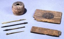 Photograph of ancient writing implements. A set of styluses, ink opt and wooden pieces of a wax tablet. 